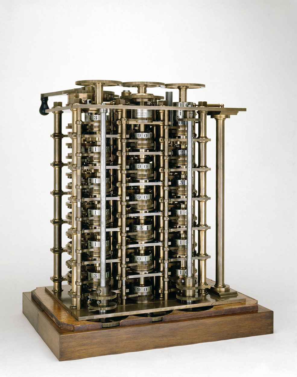 Seção da Máquina Diferencial nº 1 de Babbage: torre de engrenagens e discos numerados de latão sobre uma base de madeira, com manivela preta.
