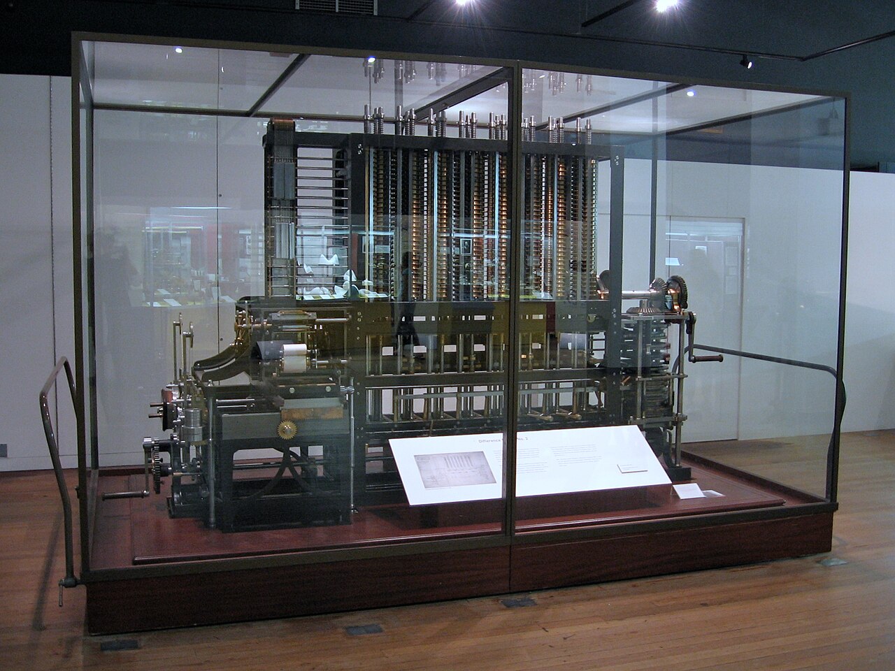 Máquina Diferencial nº 2 de Babbage dentro de uma vitrine de vidro no Science Museum: colunas de engrenagens de metal, mecanismo de impressão e manivela.
