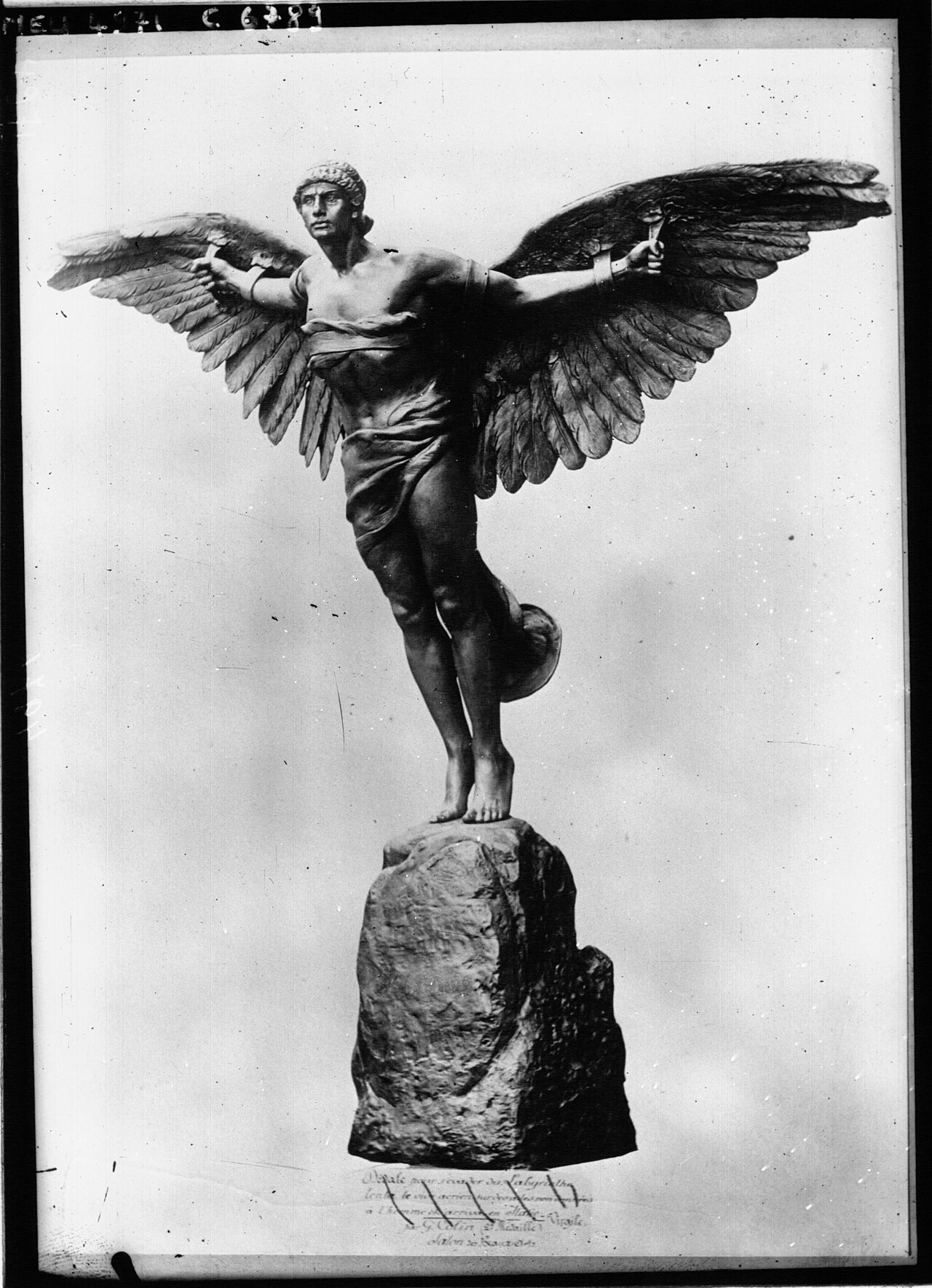 Fotografia em preto e branco da escultura de Ícaro, um homem alado de braços abertos, em pé sobre uma pedra.