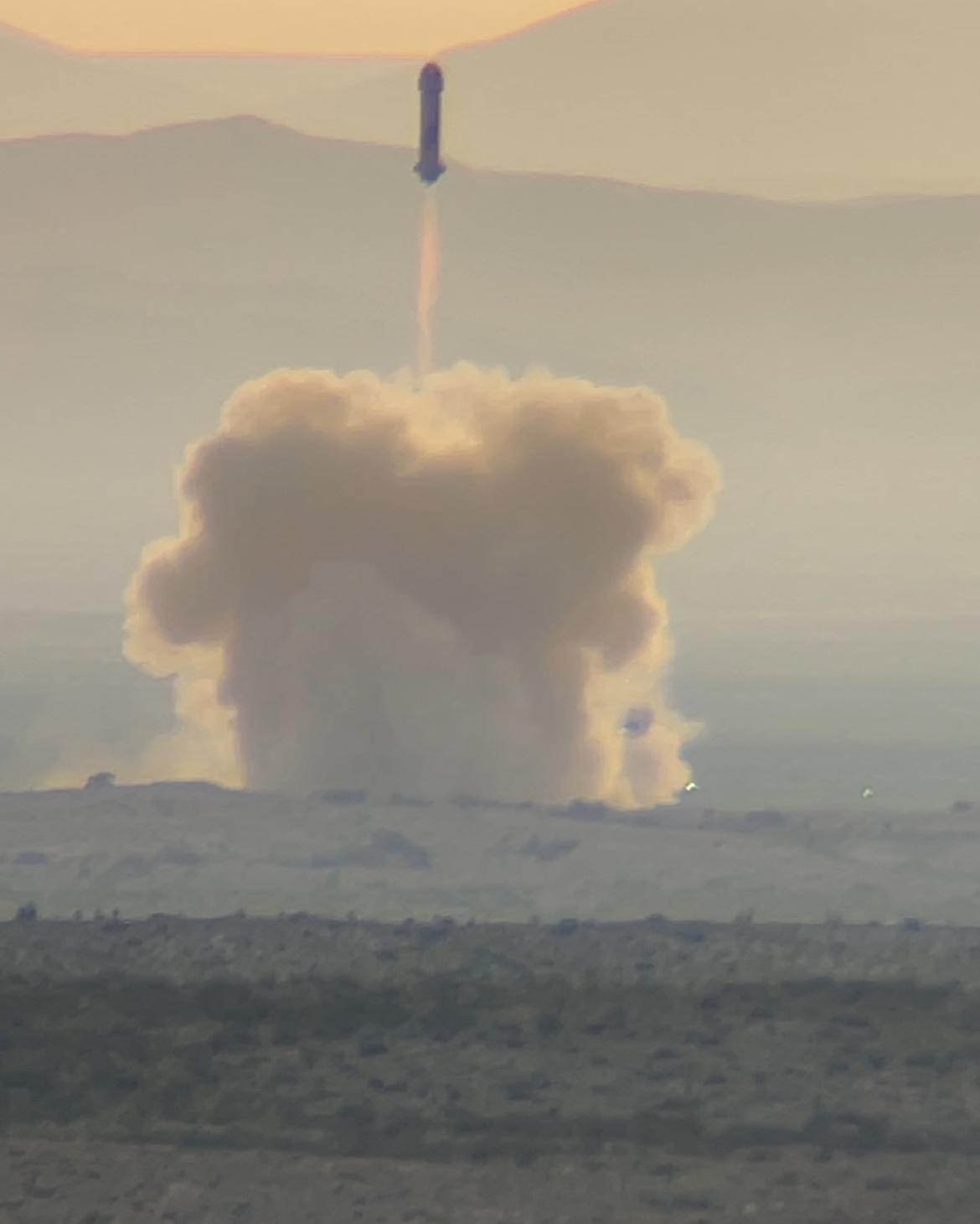 Foguete New Shepard no alto do céu, deixando um rastro de fogo sobre uma grande nuvem de poeira no deserto do oeste do Texas, ao pôr do sol.