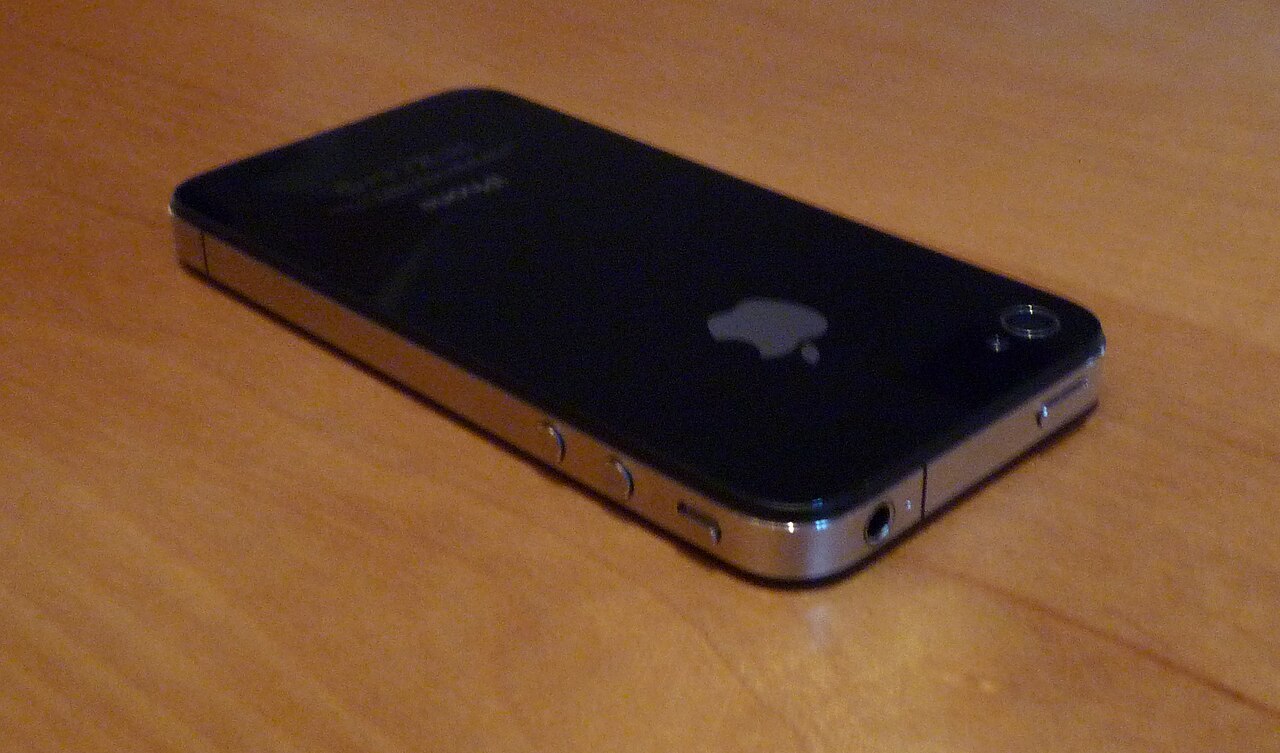 Parte traseira e laterais de um iPhone 4, de vidro escuro e moldura metálica, fotografado sobre fundo claro.