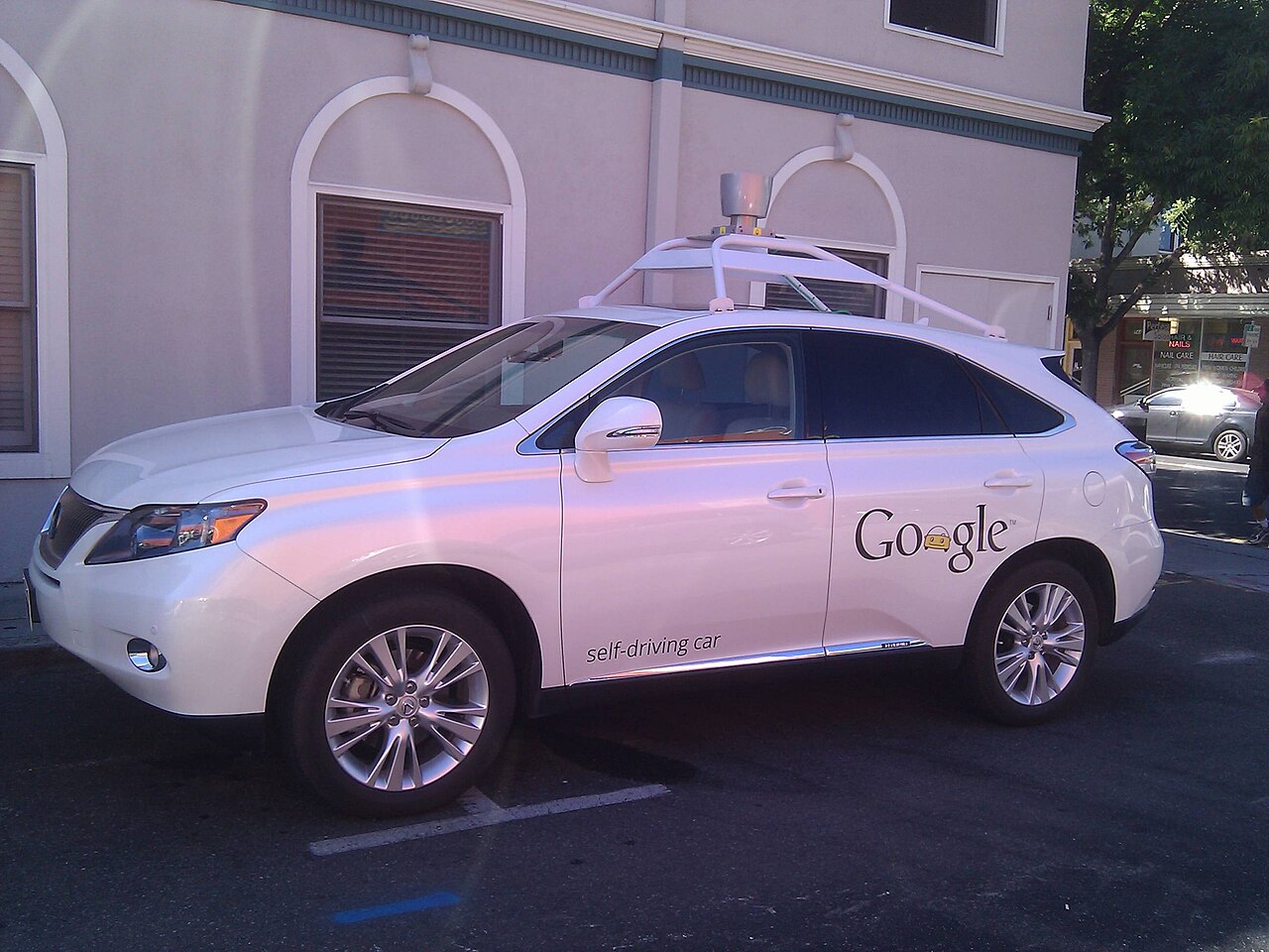 SUV branco com sensor giratório no teto e a inscrição Google self-driving car na porta, estacionado numa rua de Mountain View.