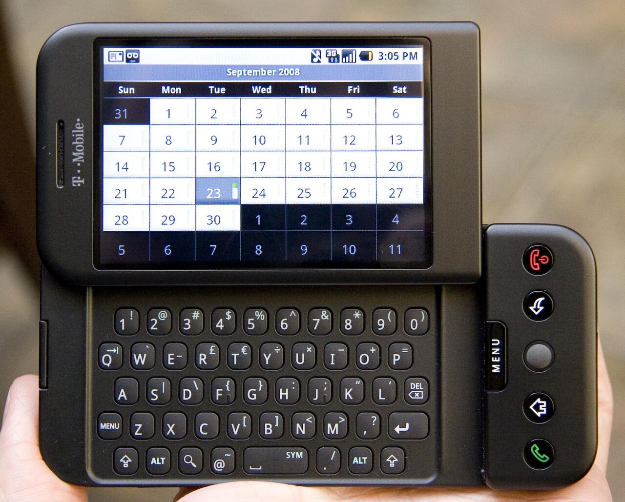Mão segurando o T-Mobile G1 com o teclado deslizante aberto e a tela mostrando um calendário de setembro de 2008.