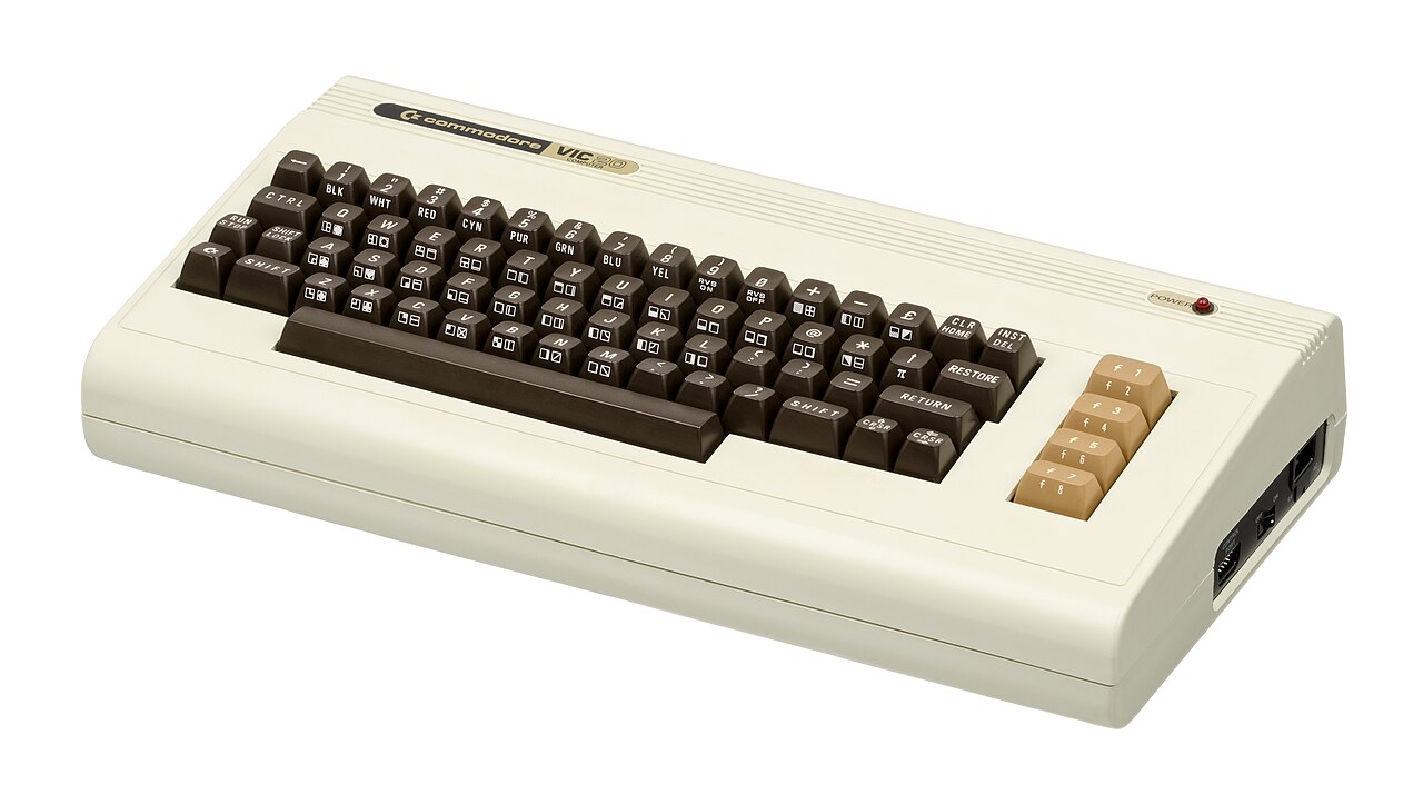 Computador Commodore VIC-20 de caixa bege, com teclado integrado de teclas marrons e cinco teclas de função mais claras, visto de cima e de lado.