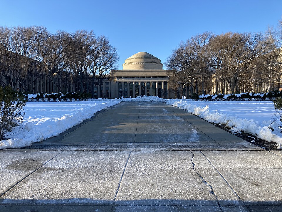 O Grande Domo do MIT ao fundo de uma esplanada, com neve dos lados e árvores sem folhas, sob céu azul.