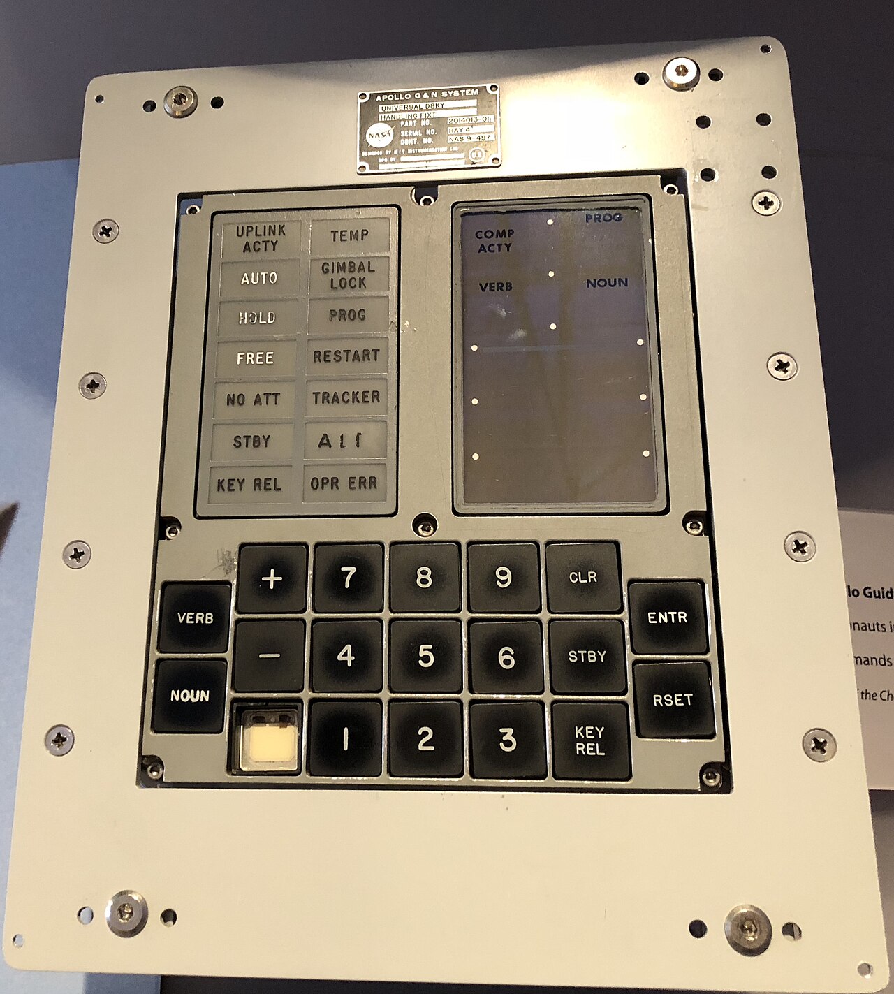 Teclado e visor do computador de orientação da Apollo, o DSKY, com teclas pretas numeradas, botões VERB e NOUN e lâmpadas de aviso rotuladas, em exposição num museu.