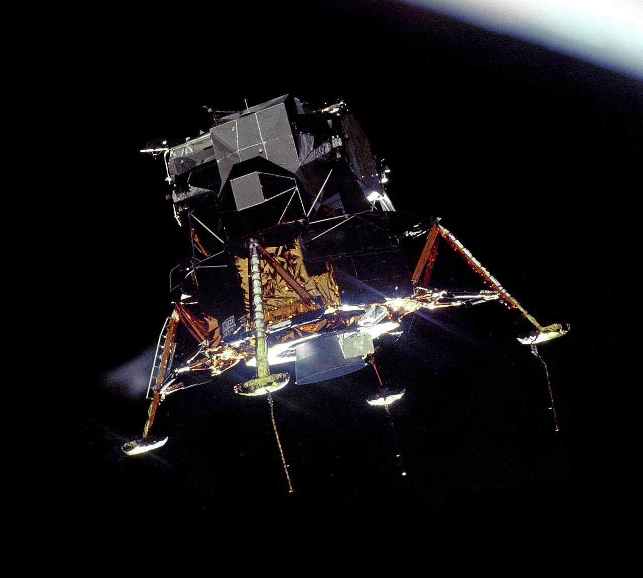O módulo lunar Eagle, dourado e prateado, com as pernas de pouso abertas, visto da órbita lunar contra o fundo escuro do espaço.