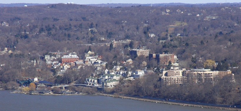 Vista do centro de Dobbs Ferry, com casas e prédios entre colinas arborizadas e a água em primeiro plano.