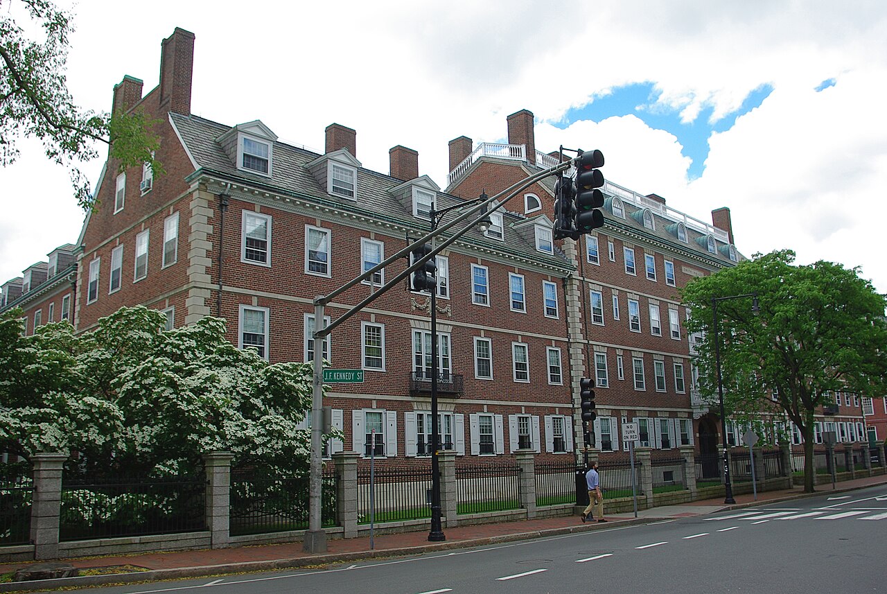 Fachada de tijolos vermelhos da Kirkland House, residência estudantil de Harvard, com árvores floridas e um semáforo na esquina.