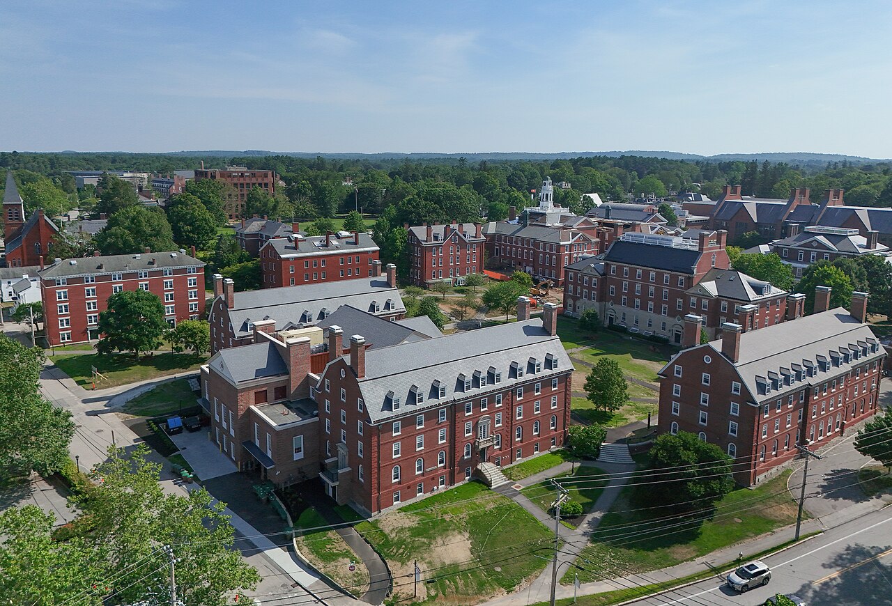 Vista aérea do campus da Phillips Exeter Academy, com prédios de tijolos vermelhos entre árvores, em dia de céu azul.