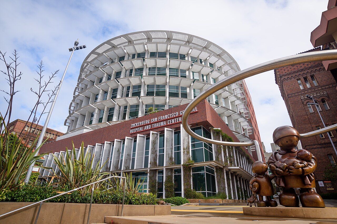 Fachada curva de vários andares do Zuckerberg San Francisco General Hospital, com uma estátua de bronze de mãe e crianças em primeiro plano.