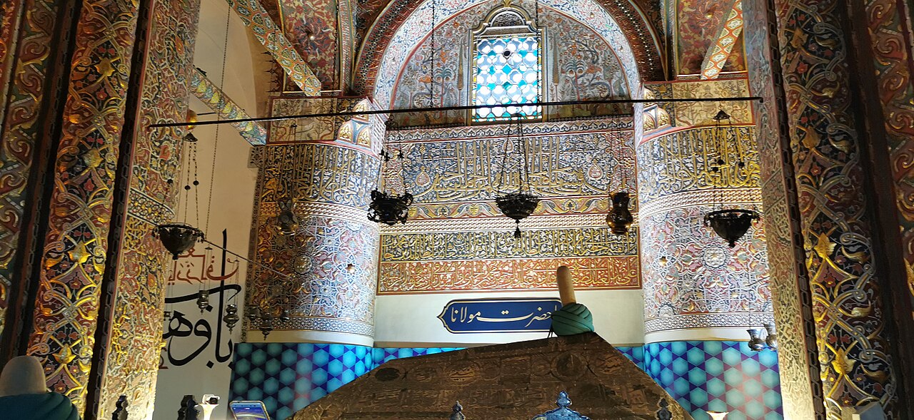 Interior ricamente decorado do Museu Mevlâna, em Konya, com arabescos dourados, caligrafia, lustres e um sarcófago coberto com tecido bordado.
