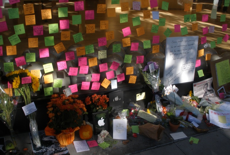 Vitrine de uma loja da Apple coberta de bilhetes adesivos coloridos e flores deixados por pessoas em homenagem a Steve Jobs.