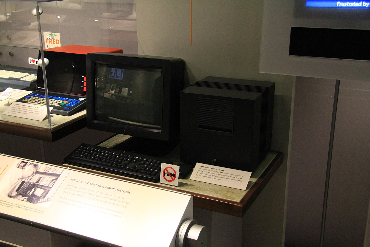 Computador NeXT em forma de cubo preto, exposto em uma vitrine do museu, com o monitor e o teclado ao lado.