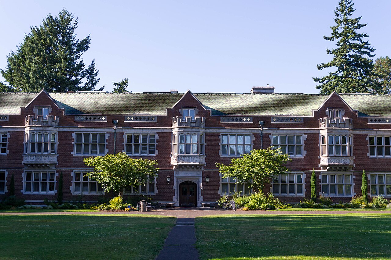 Fachada de tijolos do Eliot Hall, prédio histórico do campus do Reed College, em Portland, vista de uma alameda arborizada.