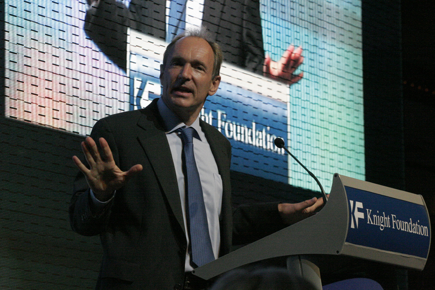 Tim Berners-Lee de gravata falando com a mão erguida num púlpito da Knight Foundation, com um telão ao fundo.